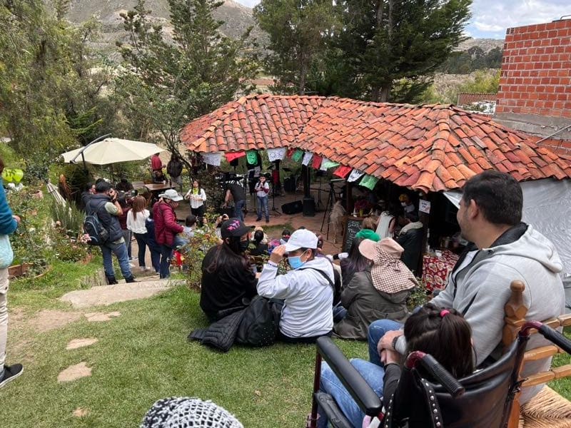 Evento de día bajo el parrillero, con papel picado y público en el pasto.