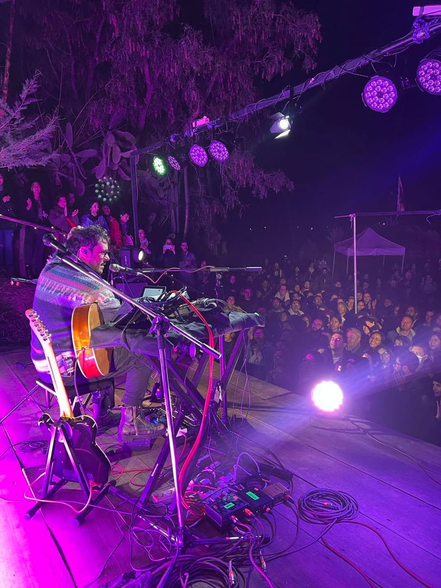 Músico con chelo en el escenario, con luces violetas.